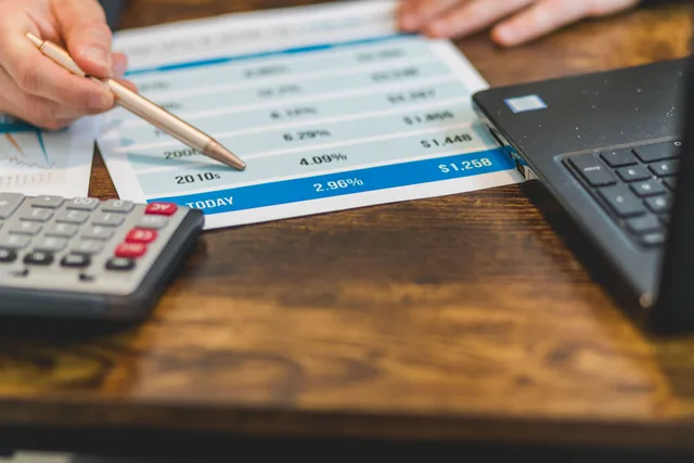 Close-up of a hand with pen analyzing financial rates on paper with a calculator and laptop nearby. Product-led traction benchmarks hold up only with internal cohorts, not borrowed numbers
