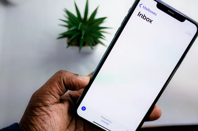 A close-up view of a smartphone screen displaying the email inbox, held by an adult's hand. Startup email marketing: commercial or transactional?
